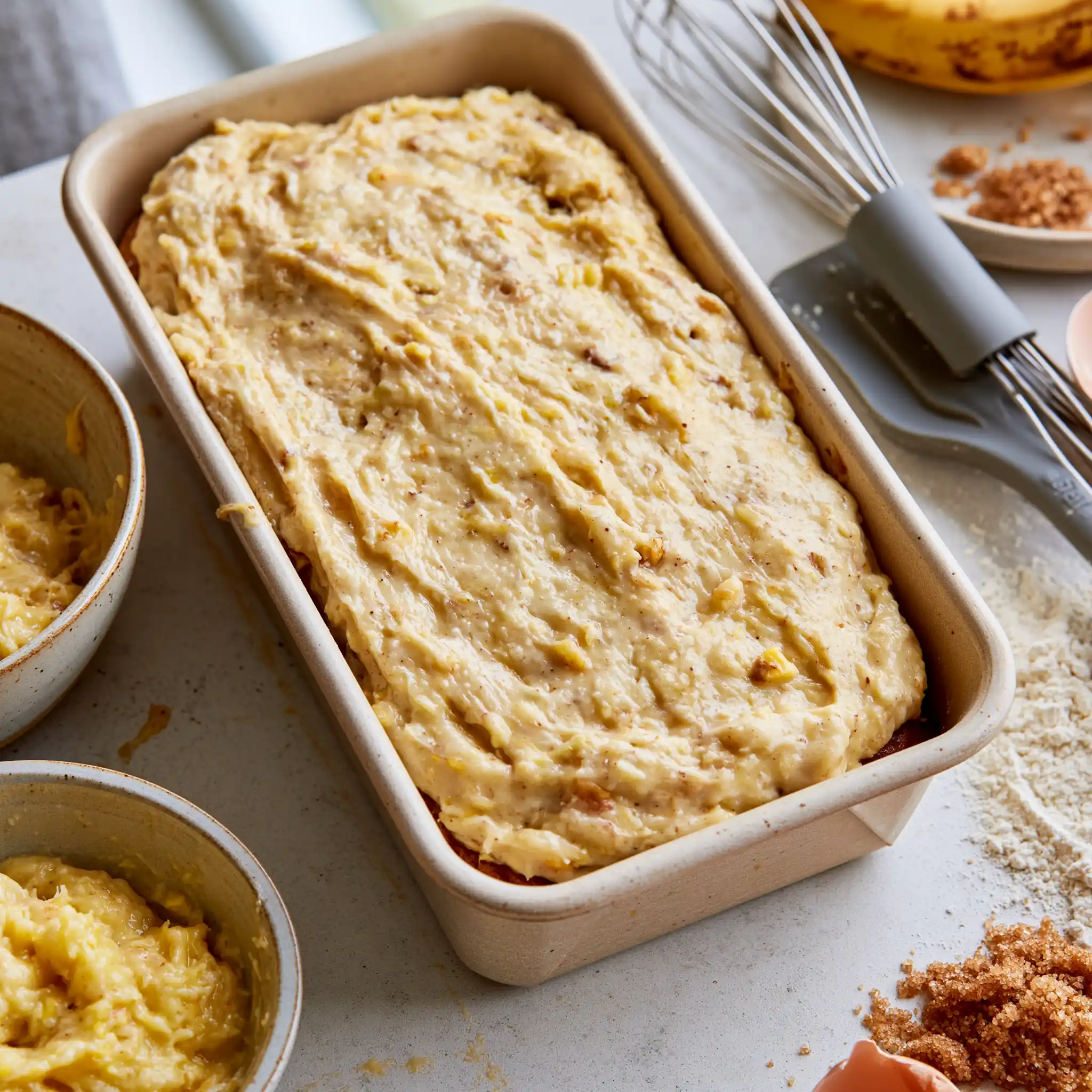 Banana bread batter being prepared and transferred to a parchment-lined loaf pan