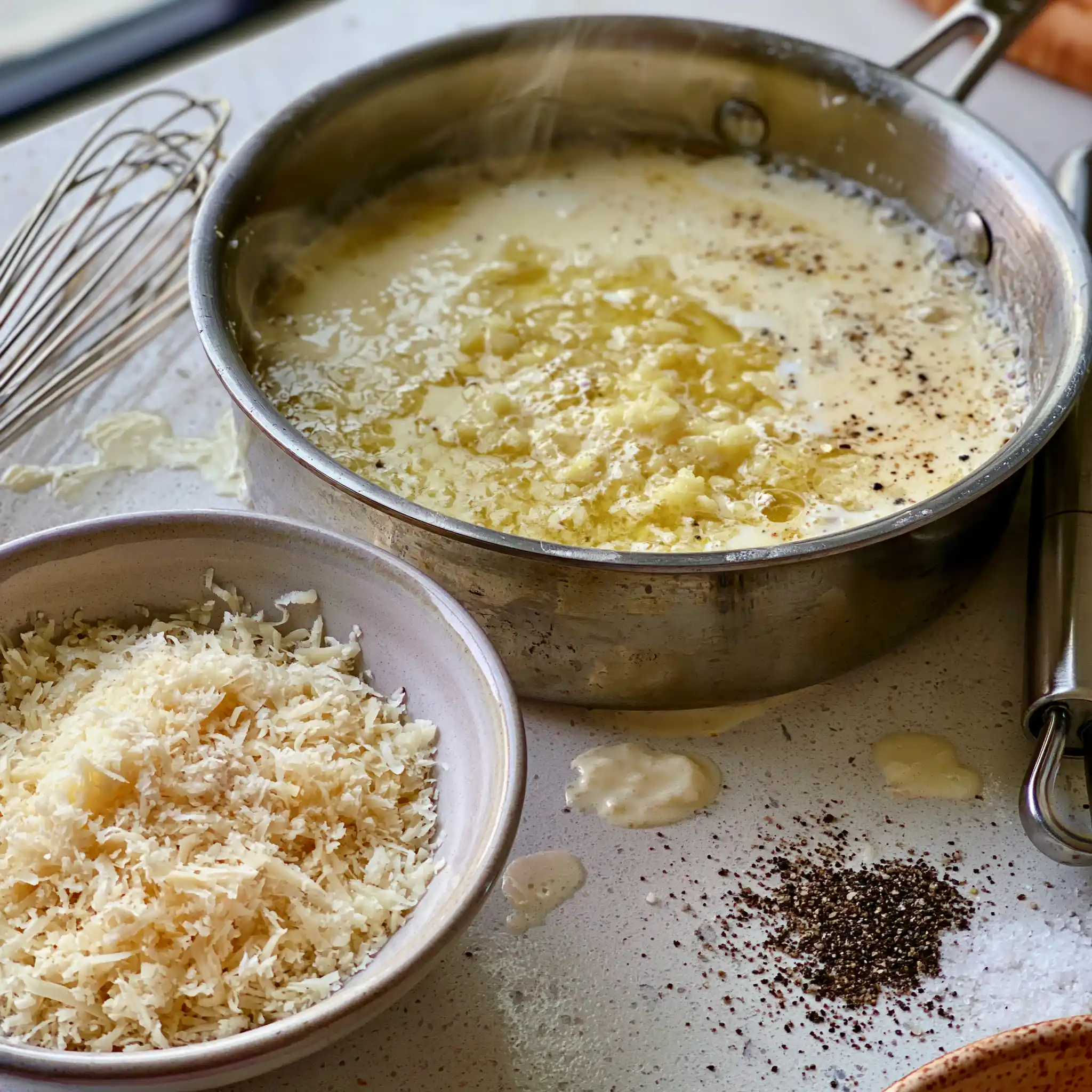 Creamy Alfredo sauce being prepared in a skillet with butter, cream and freshly grated Parmesan